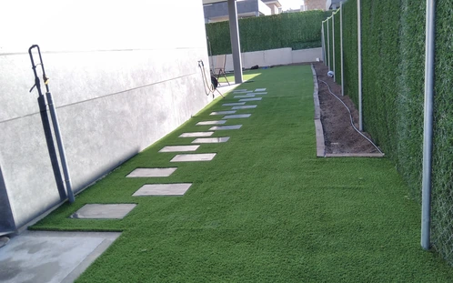 Paso de losetas sobre césped entre un muro y un cerramiento vegetal