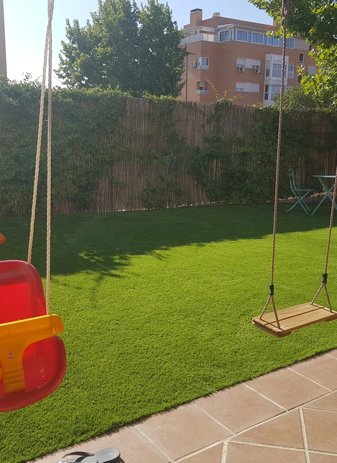 Zona de césped artificial con un columpio junto a una terraza