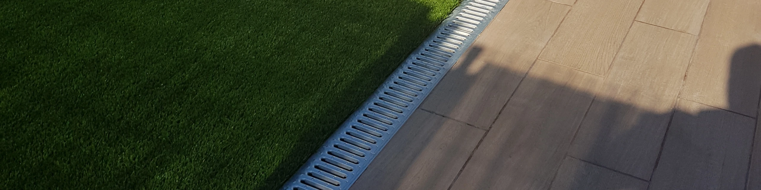 Césped artificial junto a una terraza de madera y un canal de drenaje