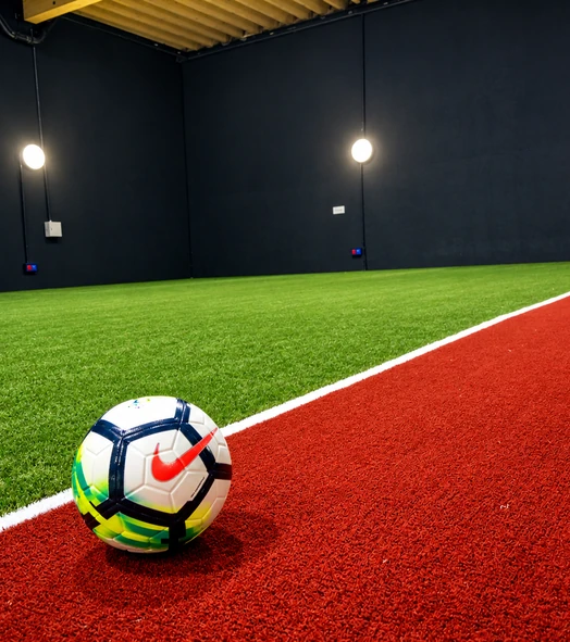 Balón sobre césped artificial junto a una banda roja en un centro deportivo