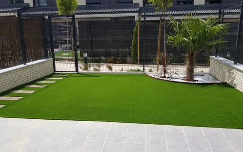Jardín con césped artificial junto a un cerramiento y terraza