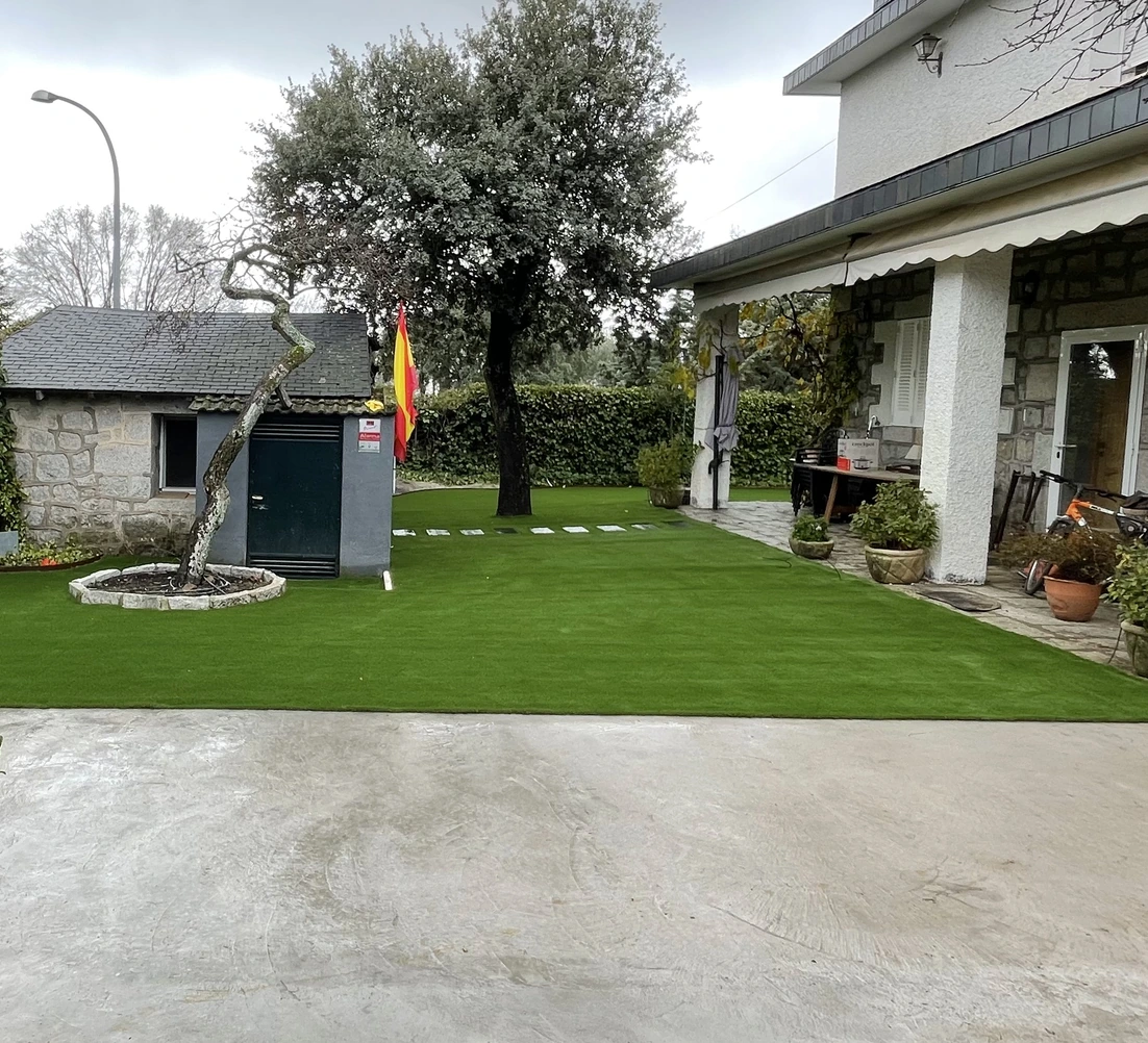 Jardín con césped artificial, olivo y pavimento junto a una vivienda