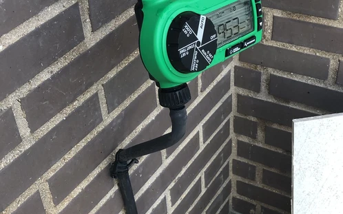 Grifo exterior con soporte de manguera en una pared de ladrillo