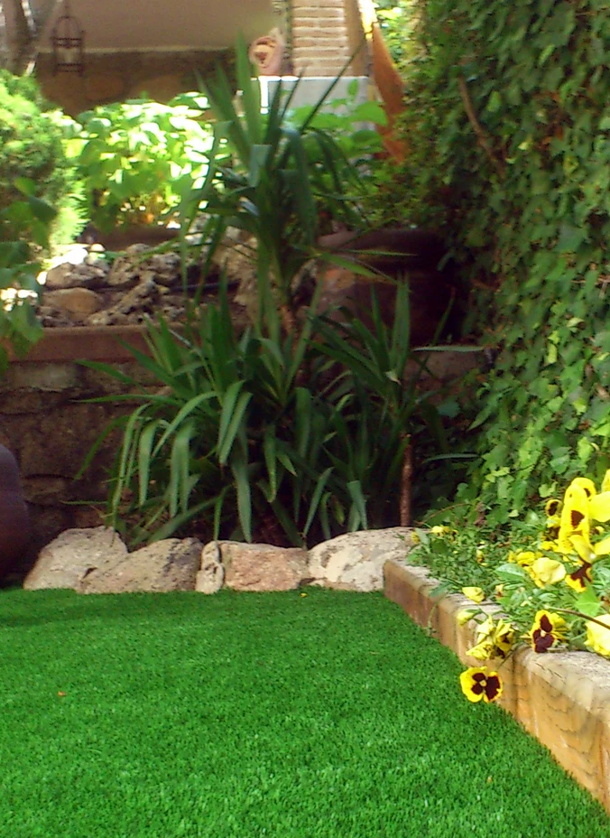 Césped artificial junto a un parterre de plantas y flores