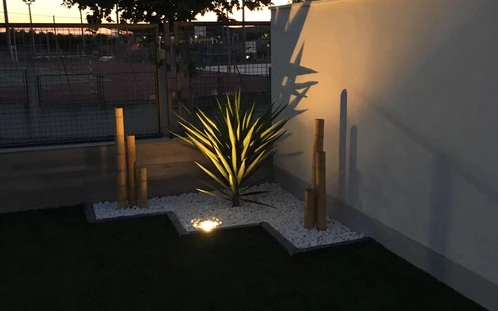 Foco de jardín iluminando una planta junto a una pared
