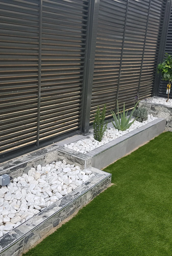 Parterre de grava blanca con arbustos junto a una valla