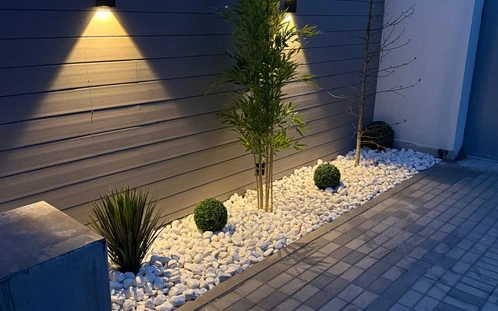 Iluminación cálida de un parterre de grava con arbustos