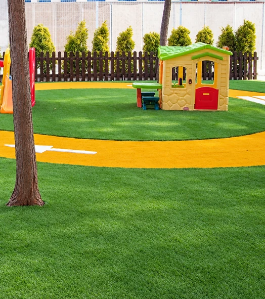 Zona de juegos con césped artificial, circuito de colores y una casita infantil