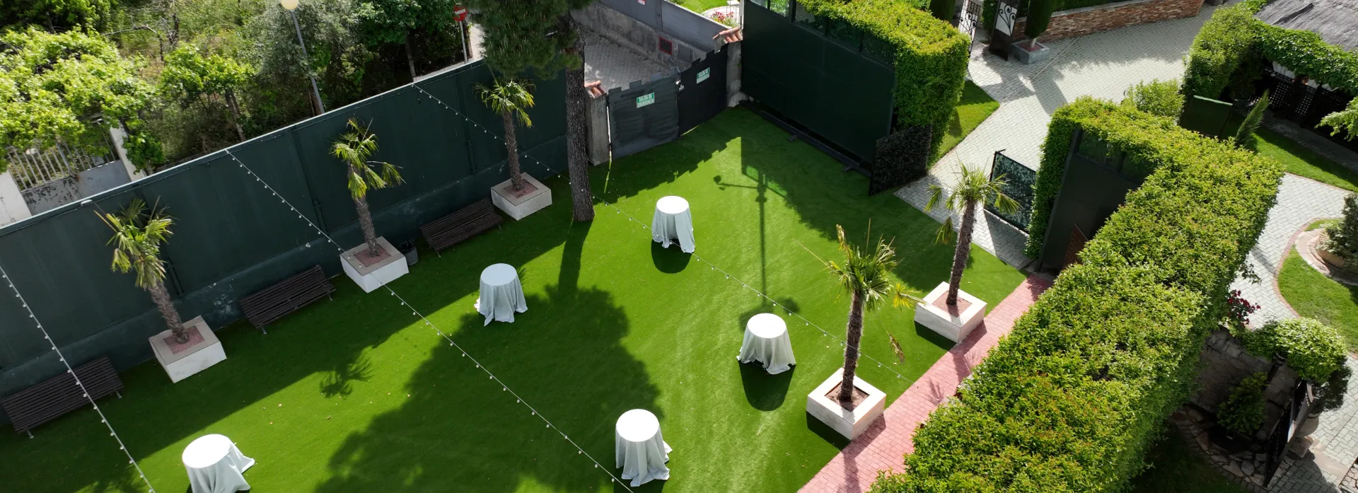 Jardín con césped artificial, palmeras y mesas visto desde arriba